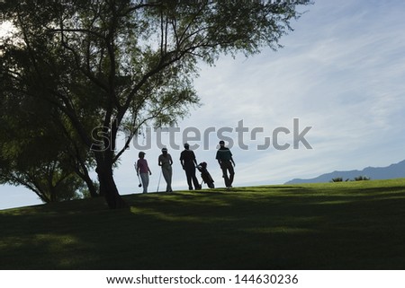 Group of silhouette golfers walking by tree on golf course