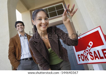 Happy couple with keys to new home by sold signboard