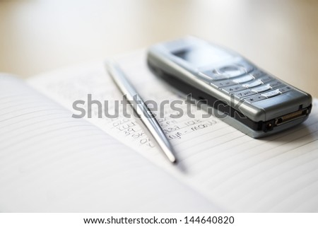 Still life of mobile phone and silver pen resting on notebook