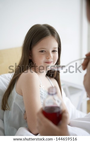 Mother giving cough syrup to daughter in bed