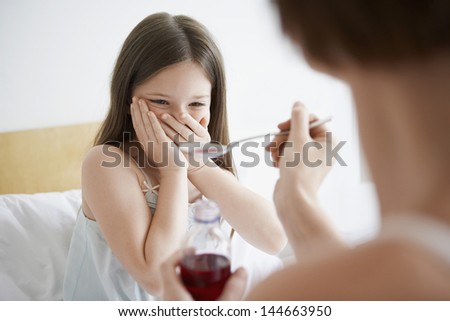 Mother giving cough syrup to reluctance daughter in bed