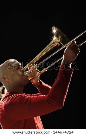 Closeup side view of an African American man playing the trombone against black background
