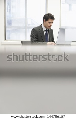 Businessman sitting at desk in office and using laptop