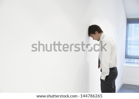 Side view of an unhappy businessman resting head against office wall