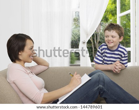 Mother writing notes as young son watching her at home