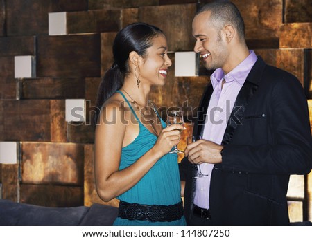 Side view of a smiling couple standing face to face with drinks in bar