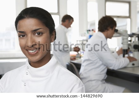 Portrait of happy female scientist with colleagues working in background