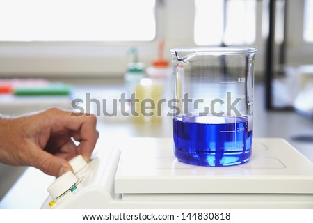 Human hand analyzing scientific glass container filled with blue liquid on scale