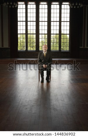 Full length of middle aged businessman sitting on chair in an empty room