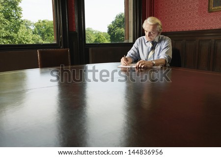 Senior businessman writing on book at conference table