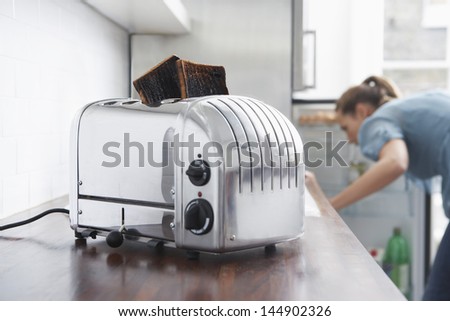 Burned toasts in toaster on kitchen counter with woman in background
