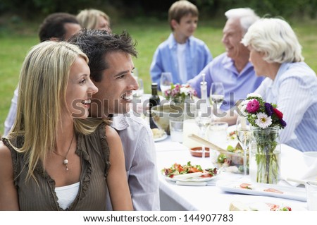 Happy loving couple at dining table with family in background
