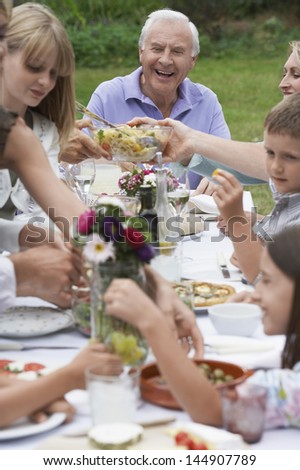 Cheerful senior man with family dining together in garden