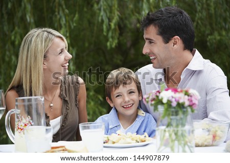 Happy young boy with parents looking at each other while sitting at dining table in garden