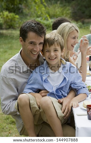 Portrait of son sitting on father\'s lap while dining with family in garden