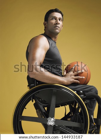 Side view of a confident paraplegic athlete in wheelchair holding basketball against yellow background
