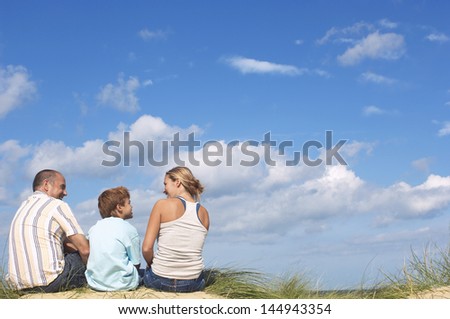 Rear view of parents and son sitting on sand and looking at eachother on beach