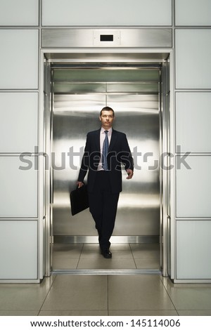 Front view of middle aged businessman with briefcase coming out from elevator