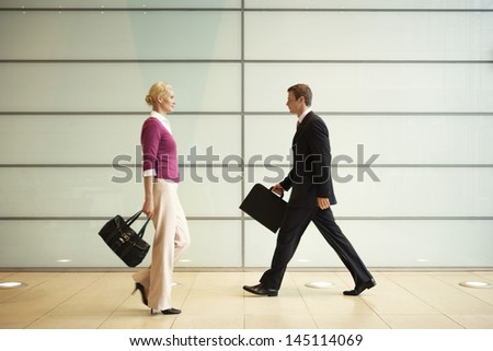 Profile shot of businesspeople with handbags walking in office corridor