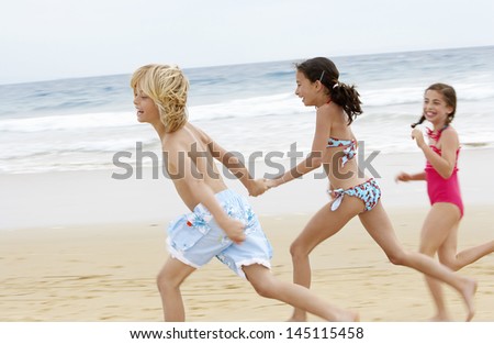 Side view of cheerful little friends running together on beach