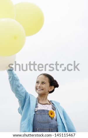 Happy cute little girl holding balloons while standing against clear sky