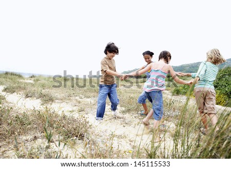 Happy little friends playing ring around the rosy on a grassy beach