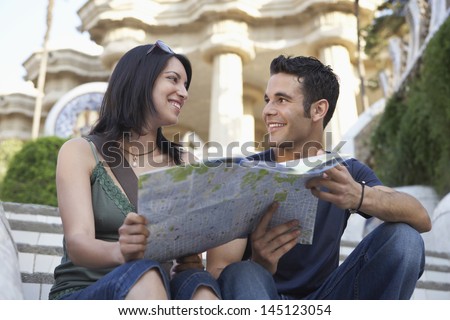Happy young couple looking at each other while holding map on steps