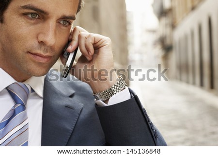 Serious young businessman using mobile phone in street