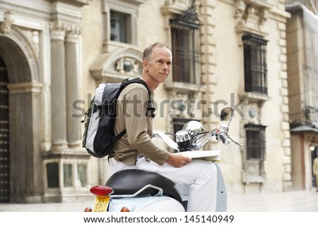 Middle aged man on scooter with map in front of building