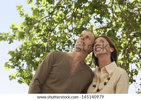 Low angle view of happy middle aged couple under tree looking away