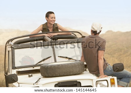 Young couple in stationary four-wheel-drive vehicle in desert