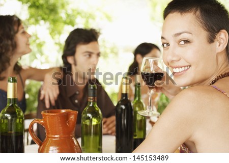 Portrait of happy young woman enjoying red wine with friends in background