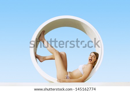 Side view portrait of excited young woman lying in tube shaped structure against clue sky at resort