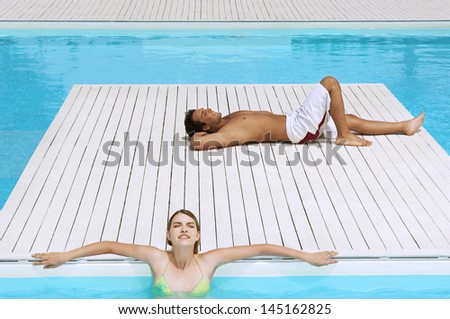 Young man and teenage girl sunbathing at poolside