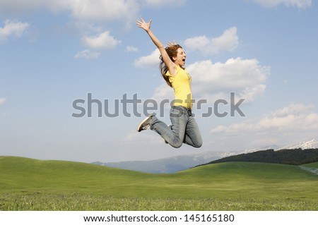 Side view of young woman with arms raised screaming while jumping in park