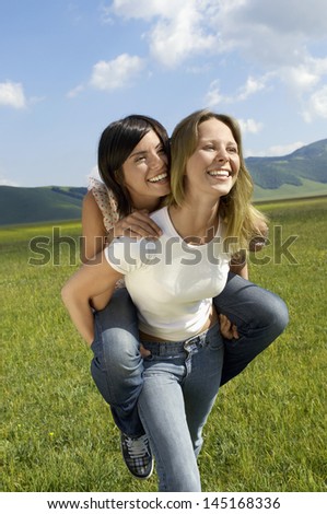Young woman giving piggyback ride to female friend in park