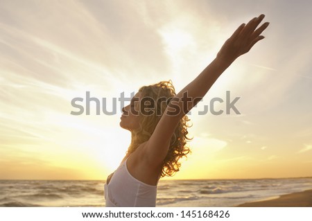 Side view of young woman with hands raised meditating at beach