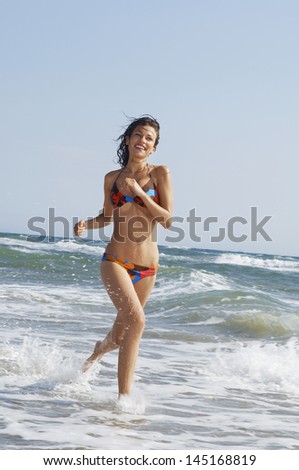 Happy young woman in bikini running in surf at beach