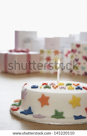 Decorated birthday cake with candle in front of cards in studio