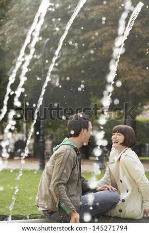 Side view of a cheerful couple laughing on fountain edge
