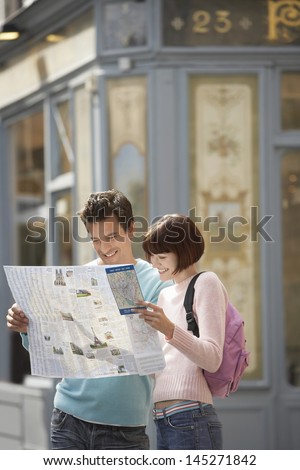 Happy young couple reading map on street corner
