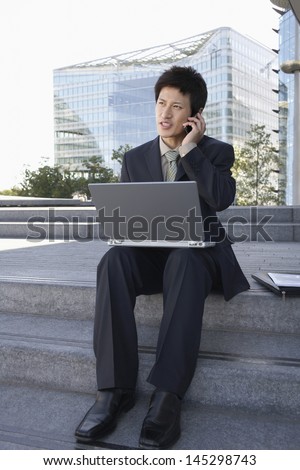 Young businessman using laptop and cellphone on outdoor steps