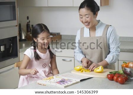 Daughter coloring on kitchen counter and mother cutting bell pepper in the kitchen