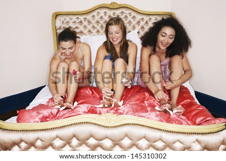 Three teenage girls in pajamas painting toenails on funky bed at slumber party