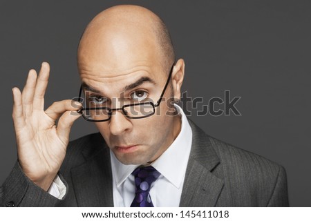 Portrait of a bald businessman with hand on glasses making a face against gray background