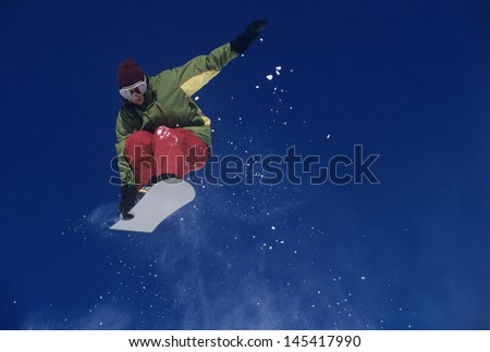 Low angle view of a male snowboarder jumping with snowboard against blue sky