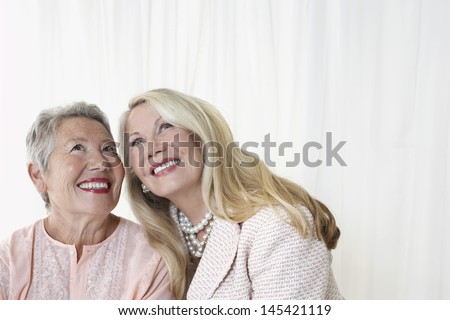 Two happy elegant senior women looking up against white background