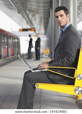 Side view of a young businessman using laptop at the train station