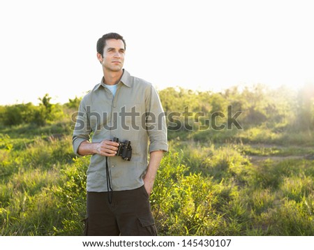 Portrait of a young man holding binoculars on meadow