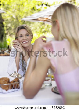 Two women sitting at outdoor dining table and talking